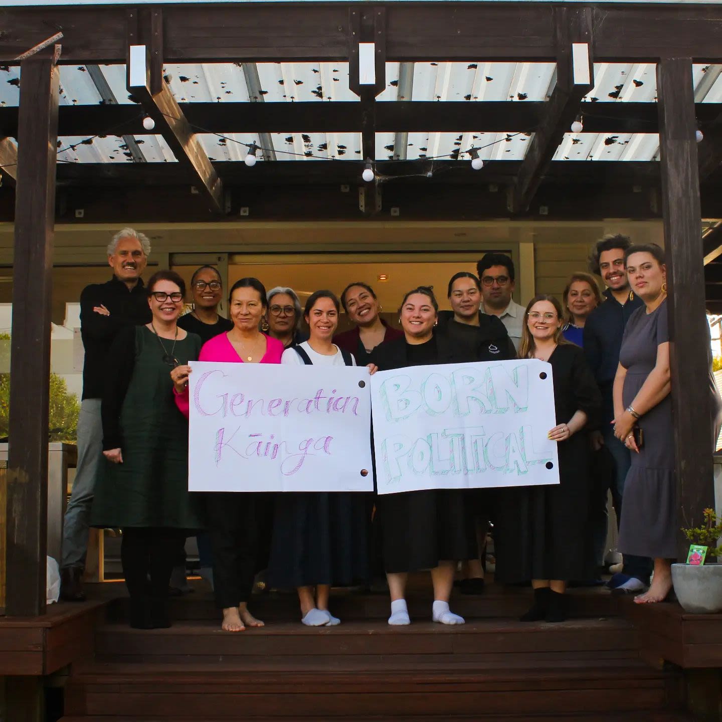 Group of people holding signs on white paper stating 'Generation Kāinga' on one, 'Born political' on another.