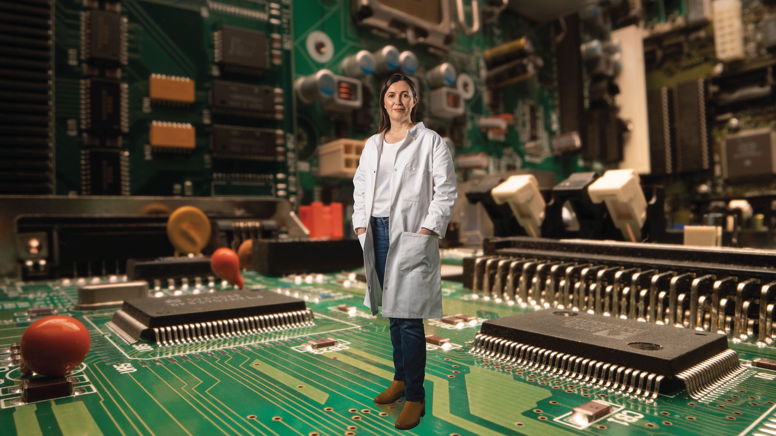 Natalie Plank in lab coat stood in a room made of circuit boards