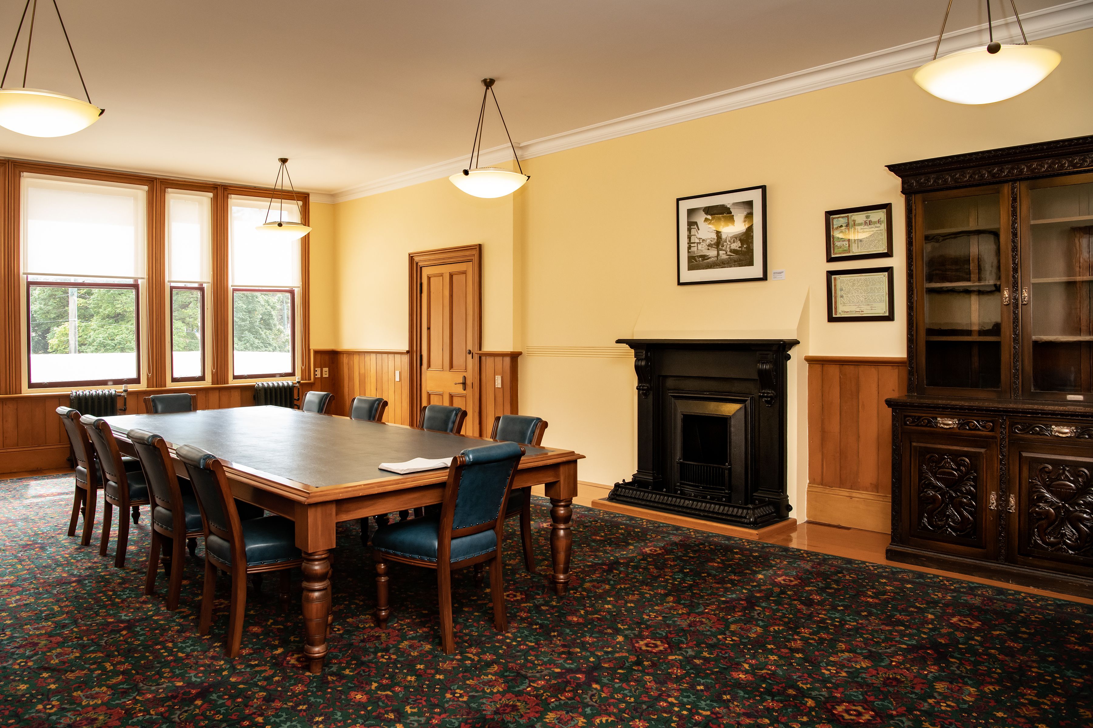 Fullsized board table with upholstered blue chairs, with fireplace, then sideboard near right of the image