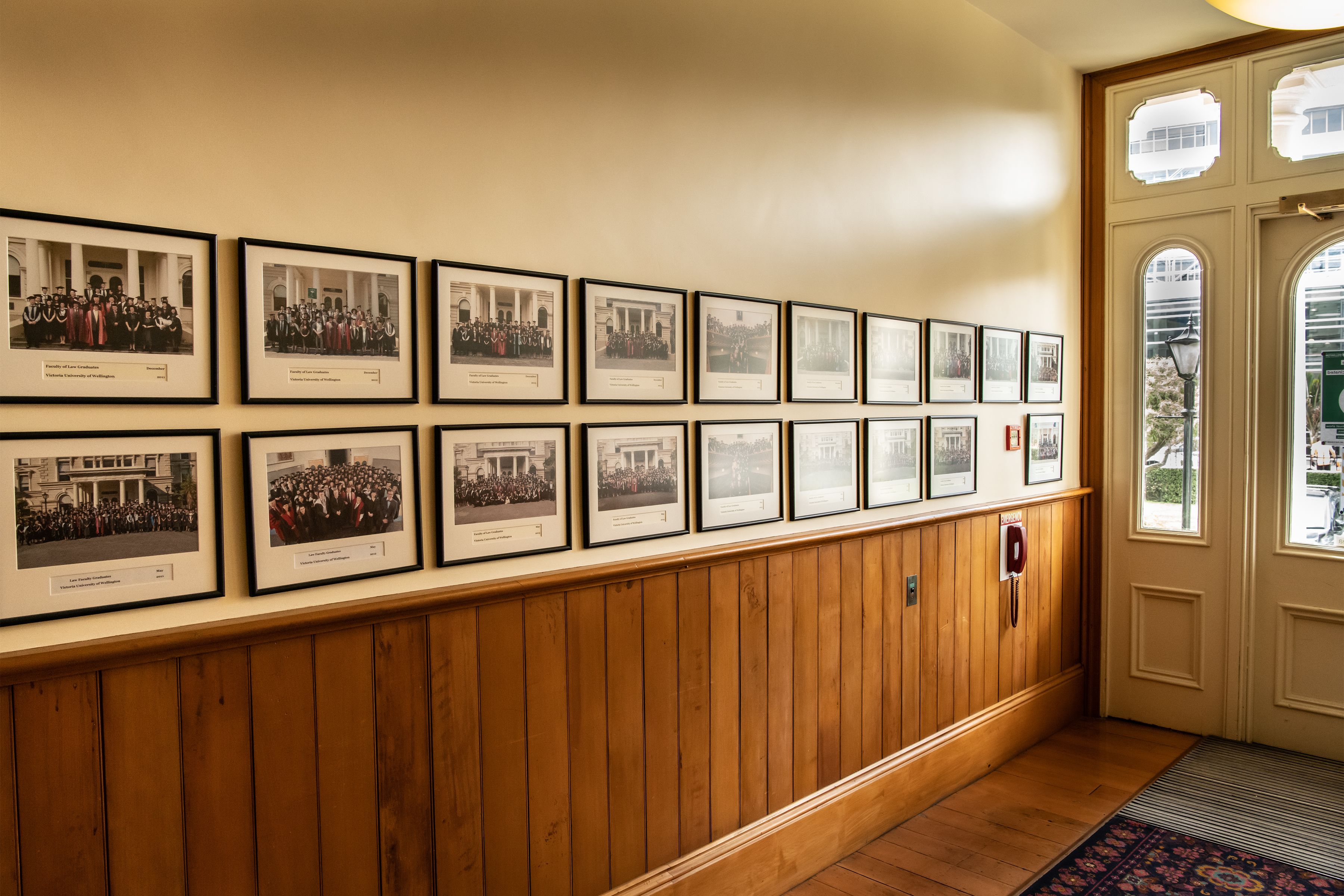 twenty framed photos with base of golden wood wall, includes a phone and a door at far right.