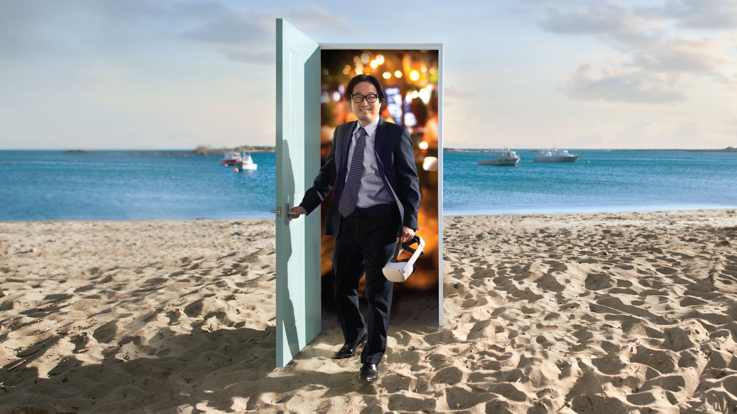 Dr Taehyun Rhee standing walking through a door from a restaurant onto a beach. He is wearing a suit and holding a VR headset