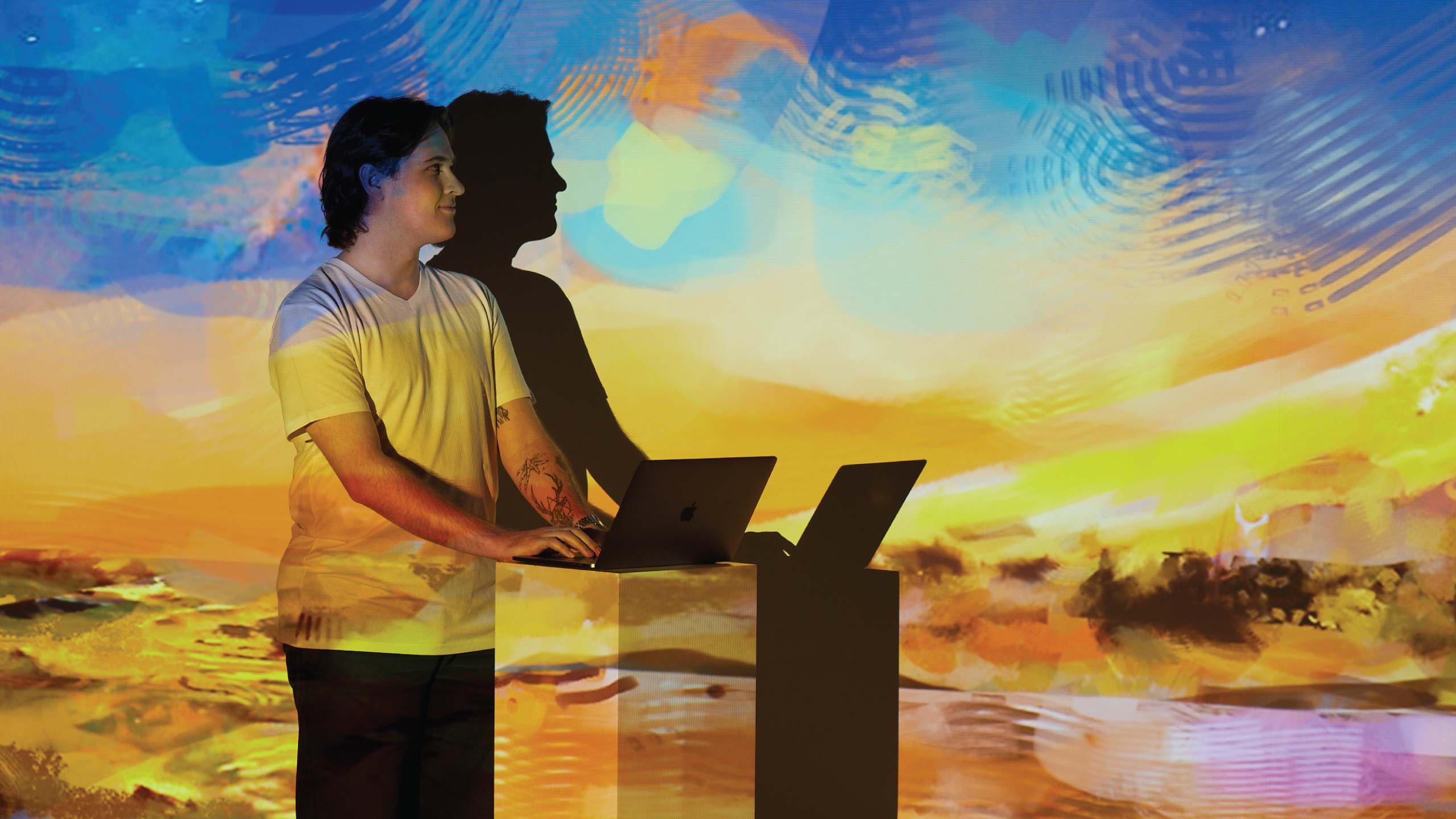 Tom Trengrove looking up from laptop as one of his digital landscape paintings is projected onto him