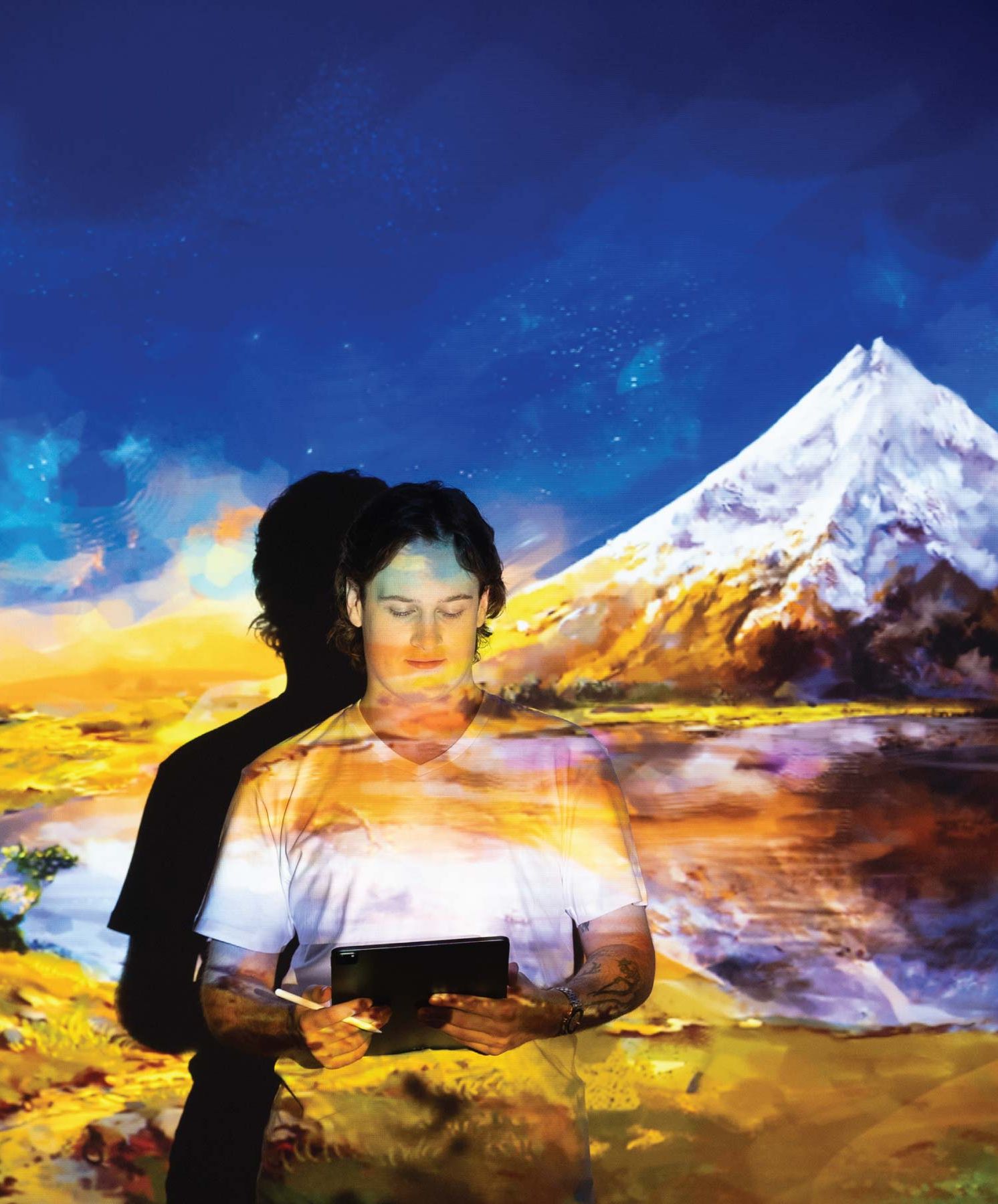 Tom Trengrove looking down at tablet with digital landscape painting projected onto him